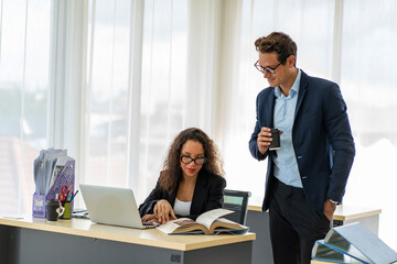  American Latino woman in a suit sits on her desk holding a cup of coffee, drinks her morning coffee for breakfast, greets her friend, a handsome male employee say hi at the company