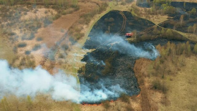 4K Aerial View Spring Dry Grass Burns During Drought Hot Weather. Bush Fire And Smoke. Fire Engine, Fire Truck On Firefighting Operation. Wild Open Fire Destroys Grass. Ecological Problem Air