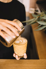 Barista pouring milk from pitcher into a cup, making latte art, close up view