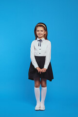 Cute attractive cheerful schoolgirl wearing uniform smiling and holding hands together, posing adorable over blue paper studio background
