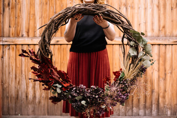 Woman holding huge hand made wreath made of grape veins, decorated with dry flowers, cropped photo