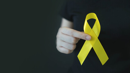 World suicide prevention day. Human hands holding yellow ribbon awareness symbol for preventing suicide on black background. Mental health care concept. - obrazy, fototapety, plakaty