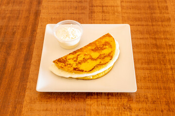 Corn cachapa filled with a good chunk of melted queso fresco and more queso fresco in a clear plastic container. Venezuelan food