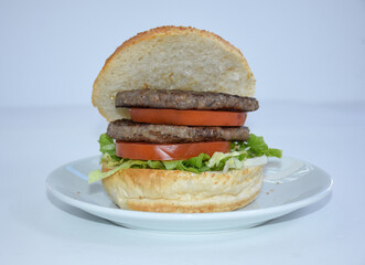 Juicy hamburger double patty with lettuce and tomato on white plate, fast food isolated