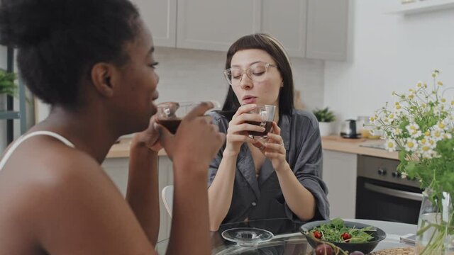 Handheld tracking with slowmo of happy queer couple smiling and chatting while enjoying coffee in cozy kitchen in morning