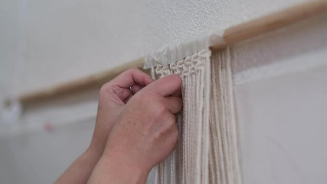 The base knots of macrame, the view from behind the shoulder close-up of the women hands, she ties knots. ECO friendly modern knitting DIY natural decoration concept.