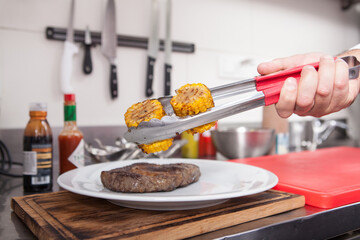 Close up of a chef adding grilled sweet corn to the plate with ribeye steak
