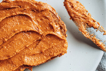 Close-up of peanut butter on toasted bread on light gray plate. Food background.