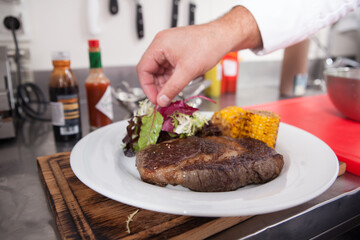 Chef adding salad to grilled beef steak and sweet corn