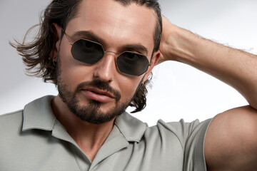 Brutal man in sunglasses, close-up, brunette with stubble in stylish glasses on a gray background