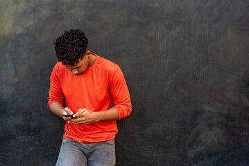 Afro latin young man using mobile phone against a wall