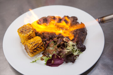 Cropped close up of blowtorch flames on grilled ribeye beef steak