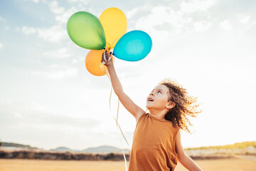 Carefree ethnic child playing with colorful balloons in field