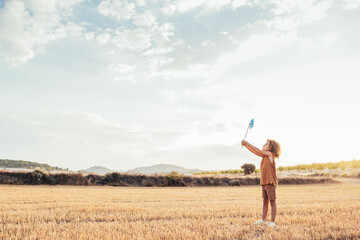 Ethnic kid playing with toy windmill in dried field