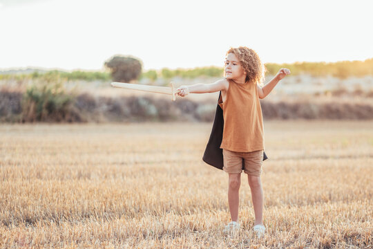 Ethnic child in knight costume with sword in field