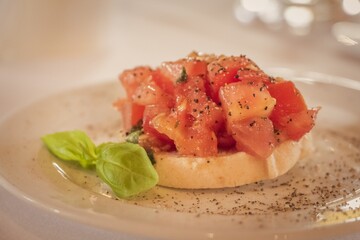 Delicious starter bruschetta with baguette tomato and basil. Premium menu appetizer. The classic italian food is served on a white plate