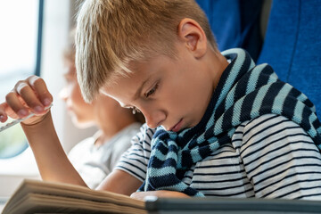 Happy children travels on train returns to home from holidays. Boy prepare to Back to school. Thoughtful Boy reads book. Happy girl sits by window in background
