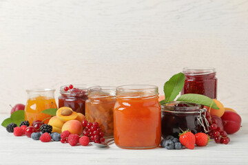 Fototapeta na wymiar Jars with different jams and fresh fruits on white wooden table