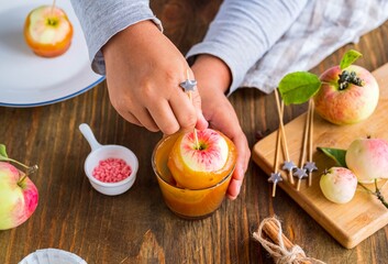 Step-by-step recipe, a boy in a gray long sleeve dips whole apples on skewers in caramel. Children's desserts, party.