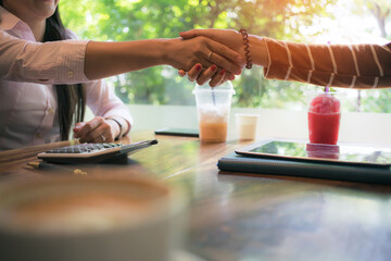 Fototapeta na wymiar asian business woman staking hand, together create a mutually beneficial business relationship. Economic graph on tablet the table, Meeting point at the coffee shop