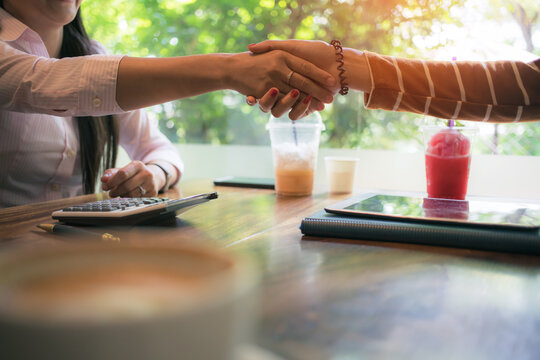 asian business woman staking hand, together create a mutually beneficial business relationship. Economic graph on tablet the table, Meeting point at the coffee shop - Powered by Adobe