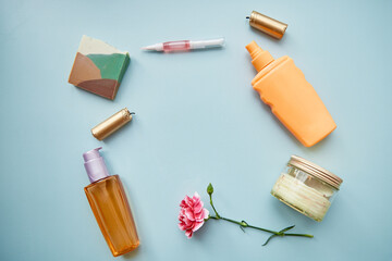 Beauty cosmetic products top view copy space: natural oil, eye patches, natural soap, cosmetic bottle mock up on blue background with pink flower decorations. Teal and orange.Copy space