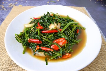 Stir fried morning glory on white plate on sackcloth on black background.