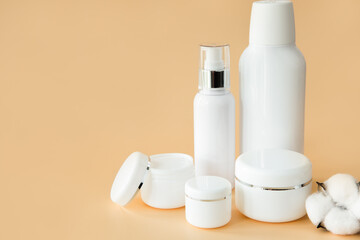 Empty white cosmetic containers and bottles on a beige background. A set of cosmetics for face and body care. Copy space.
