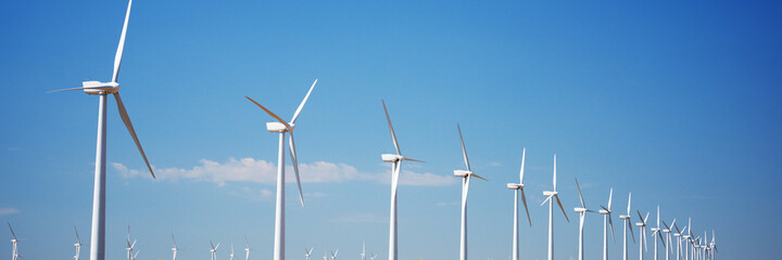 Fototapeta premium Wind turbines in the row against a blue sky. Panorama