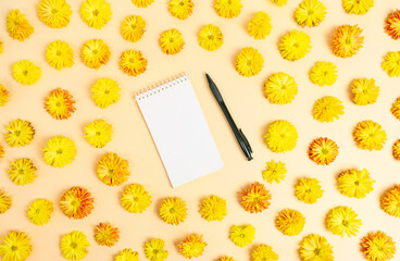 White notebook for notes with pen in round frame made of yellow chrysanthemum flowers on light yellow background. Floral natural pattern.