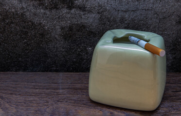 Cigarette that were burning placed on greyish green ashtray on old wooden rustic table. Copy space,...