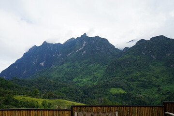 View of high green mountain and cloudy blue sky from wooden balcony