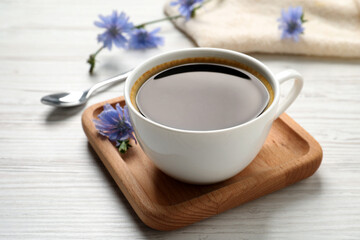 Fototapeta na wymiar Cup of delicious chicory drink and flowers on white wooden table, closeup