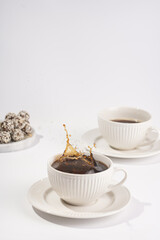 Big coffee splash in a white porcelain cup with coffee drink cappuccino on a white saucer plate on a white surface