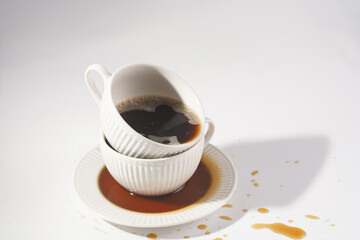 a white porcelain cup with cappuccino stacked in another mug on a white saucer plate on a white surface