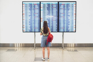 young woman looking on the timetable schedule list before the flight in airport