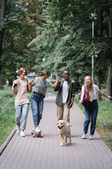 Positive interracial teenagers having fun with retriever and skateboard