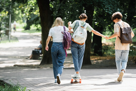 Teen Boy Holding Hand Of Friend On Skateboard In Park