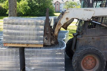 A small tractor lifts a pallet with concrete bricks. Street reconstruction.
