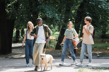 Smiling african american boy holding retriever on leash near friends in park