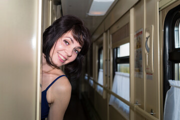 A happy brunette woman looks out of the compartment car and looks curiously into the corridor