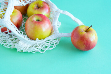 Red-yellow ripe juicy apples in a handmade mesh on a green background. Environmental concept. Side view. selective focus