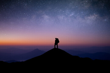 Silhouette of young man traveler with backpack standing and watched the star and milky way alone on top of the mountain. He enjoyed traveling and was successful when he reached the summit.
