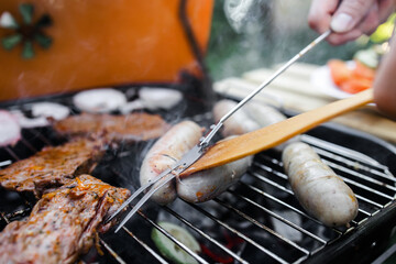 View of the grill with sausages and vegetables. The sausages are turned over with a metal fork. Spend time with your family at the grill. Social meetings, friends. Red grill with kindling