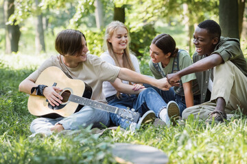 Interracial teenagers with acoustic guitar doing fists bump in park