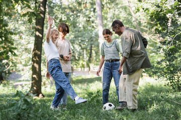 Obraz premium Cheerful multiethnic teenagers playing football in park