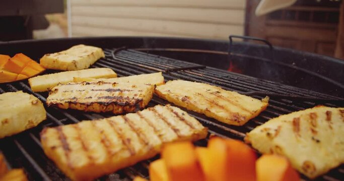Fresh mango, pineapple slices and a wheel of brie cheese in a ramekin being placed on a barbecue grill