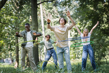 Fototapeta premium Smiling multiethnic teenagers twisting hula hoops in park
