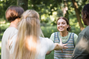 Obraz premium Blurred teenager outstretching hand near smiling multiethnic friends