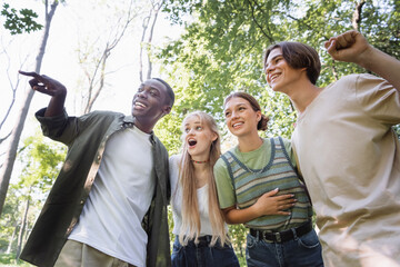 Low angle view of smiling african american boy pointing away near friends outdoors